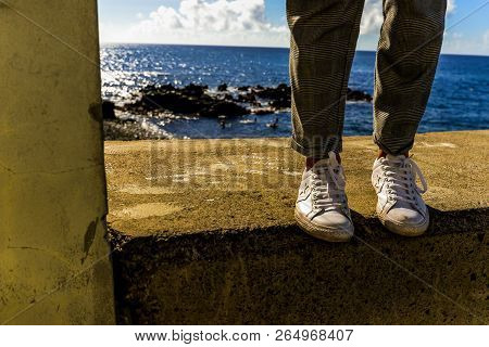 A Woman On A Ledge Next To The Ocean In Funchal - Maderia, Portugal