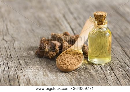 Glass Bottle Of Galangal Essential Oil, Root And Galanga Powder In Wooden Spoon On Rustic Table. Hea