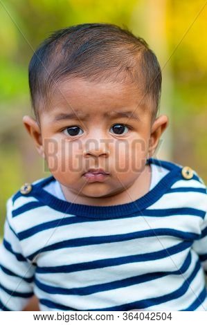 A Baby Boy Looking And Smiling. Dressed Are White And Navy Blue Striped Dress. Baby Candid Shoot. Ba