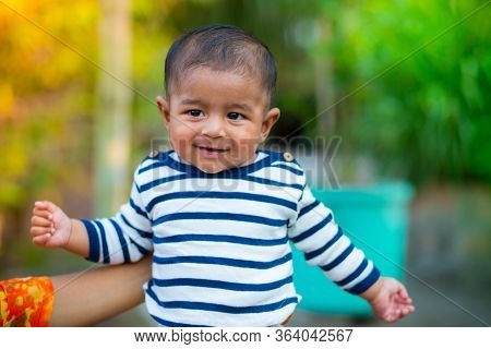 A Baby Boy Looking And Smiling. Dressed Are White And Navy Blue Striped Dress. Baby Candid Shoot. Ba