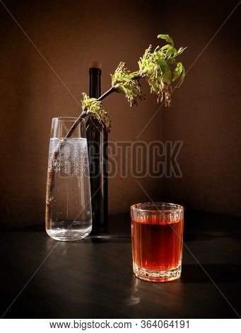 Still Life With Flowering Spring Twig Of Ash-tree With Young Leaves In A Glass Vase, Black Bottle An
