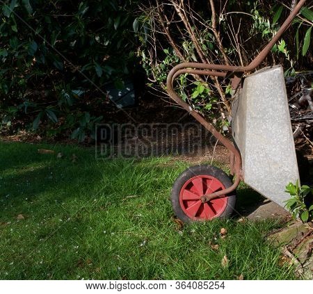 Garden Wheelbarrow With Red Wheel Standing On End Beside Grass Lawn