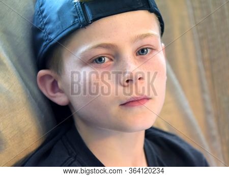 Young Boy Looks At The Camera And His Face Is Totally Expressionless.  Black Shirt And Black Cap Is 
