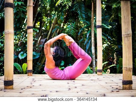 Yoga Practice Outdoor. Asian Yoga Teacher Practicing Dhanurasana, Bow Pose. Backbending Asana In Hat