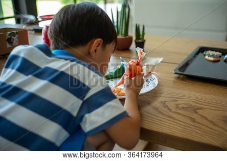 Defocused Back Portrait Of Boy Decorating The Cookie Surface By Squeezing The Liquid Sugar