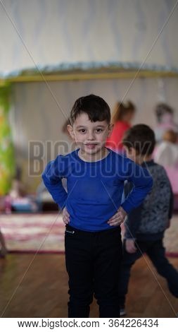 Portrait Of Cute Boy In Blue Hirt In Kindergarten. Chikd Holding Hand On His Hips And Smiling