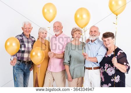 White Interior With Group Of Senior Happy Friends Holding Bunch Of Balloons