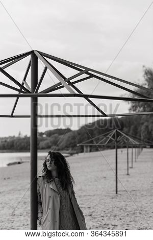 Curly Woman In The Coat Standing Near The Metal Construction On The River Bank