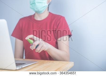 Asian Woman Wears Protective Mask Using Spray Alcohol Sanitizer Cleaning A Computer, To Prevent The
