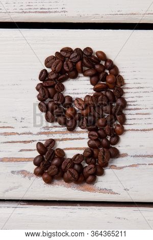 Brown Roasted Coffee Beans Arranged In A Shape Of Nine. Seeds In A Form Of Number Nine On White Wood