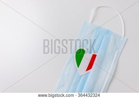 Blue Medical Protective Mask With A Miniature Italy Flag In The Shape Of A Heart. Copy Space.