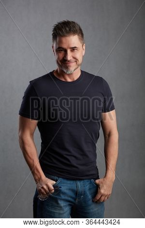 Casual older man against gray background wearing jeans and t-shirt.