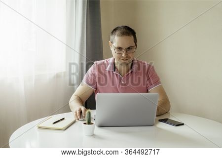 The Man Is Siiting By The Table And Working At Home On Laptop With The Phone. Man In Quarantine Work