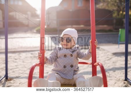 Adorable Little Girl On The Swing Set In Playground. Happy Little Girl Have Fun. One And Hulf Year G