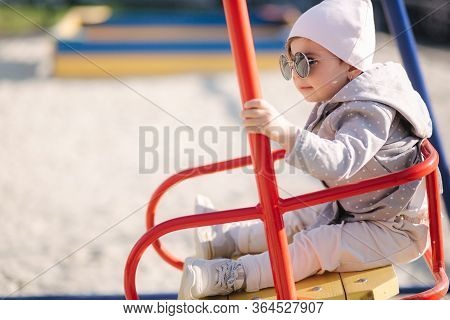 Adorable Little Girl On The Swing Set In Playground. Happy Little Girl Have Fun. One And Hulf Year G
