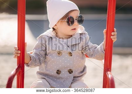Adorable Little Girl On The Swing Set In Playground. Happy Little Girl Have Fun. One And Hulf Year G