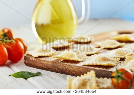Tasty Raw Ravioli With Flour, Cherry Tomatoes, Sunflower Oil And Basil On A Light Wooden Background.