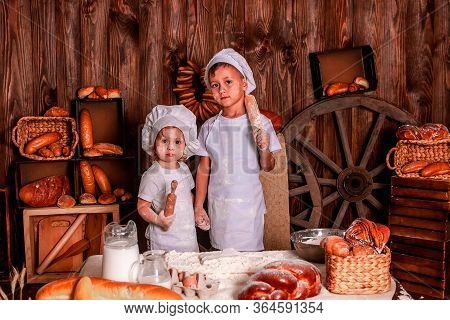 Cheerful Kids Playing Chefs And Hats Play The Role Of Baker.
The Table Is Full Of Clutter. The Mood 