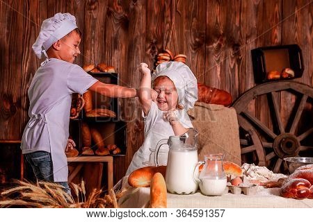 Cheerful Kids Playing Chefs And Hats Play The Role Of Baker.
The Table Is Full Of Clutter. The Mood 