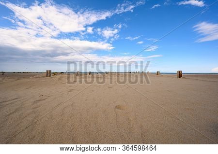 The Beach At Dunkirk With Wooden Poles Of The Sea Defences And White Clouds In A Blue Sky.