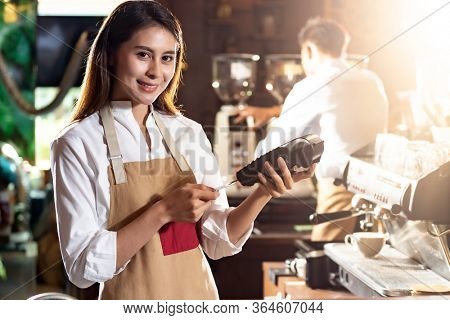 Asian Barista woman make payment with customer credit card using EMV chip technology for coffee purchase at a cafe bar. Cashless preventing from coronavirus covid-19 Spreading and infection.