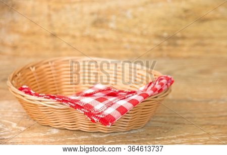 Wicker Basket With Red Checked Cotton Napkin Inside On Wooden Background