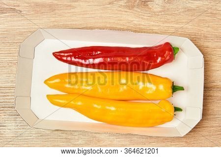 Three Pods Of Sweet Pepper, Yellow And Red, Lie In A Cardboard Tray On The Table