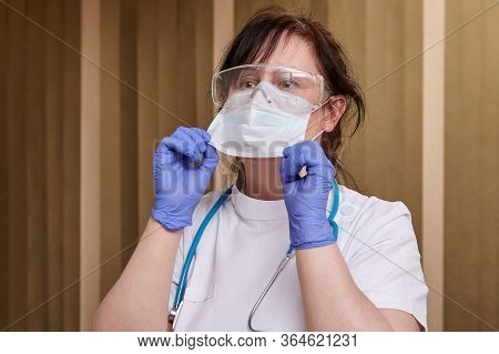 Healthcare Worker Puts On A One-time Face Mask During Covid-19 Pandemic. Caucasian Female Doctor In 