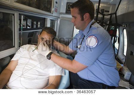 Male EMT professional helping man with oxygen mask inside ambulance