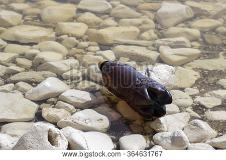 Dark Plastic Bottle On The Rocky Shore Of The River, Sea. Concept Of Pollution Of Rivers, Seas And O