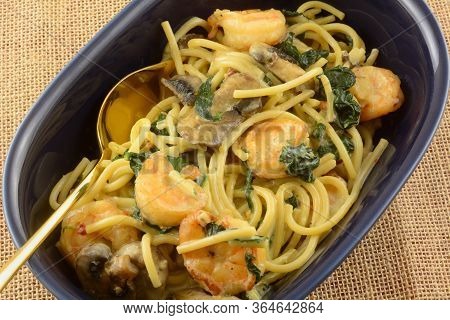 Closeup Of Shrimp And Pasta Dinner With Spinach And Mushrooms In Light Cream Sauce In Blue Serving B