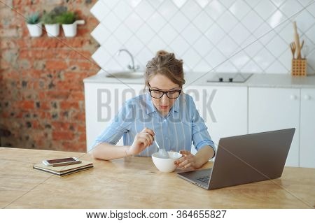 Woman Working At The Kitchen And Eating Porrige During Self-isolation. Bright Kitchen With Brick Wal