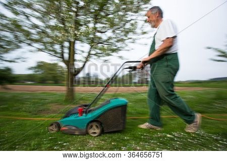 Gardener mowing the lawn - motion blurred image (color toned image)