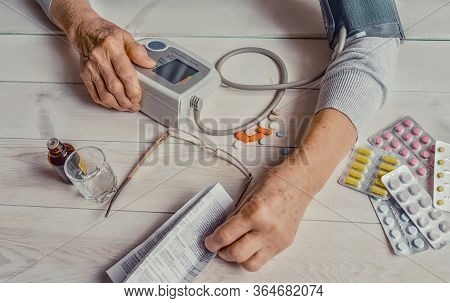 Senior Wrinkled Hand Pushing Back Pills And Thermometer, Dumb-bell On A Table. Another Old Woman Han