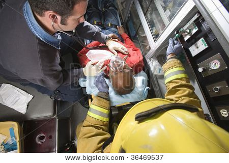 Male firefighter and EMT doctor taking care of an injured middle aged man in ambulance