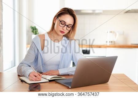 Woman Working On Laptop At Home On Kitchen. Writing On Notepad. Business Woman Thinking About Someth