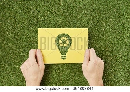 Hands Are Holding A Yellow Sheet Of Paper With An Ecological Symbol On It.