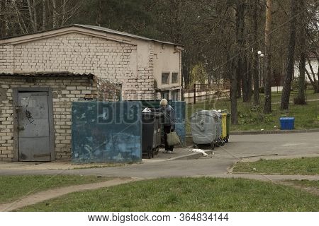 An Old Woman Pensioner Is Looking For Food And Food In The Trash. Containers For Separate Collection