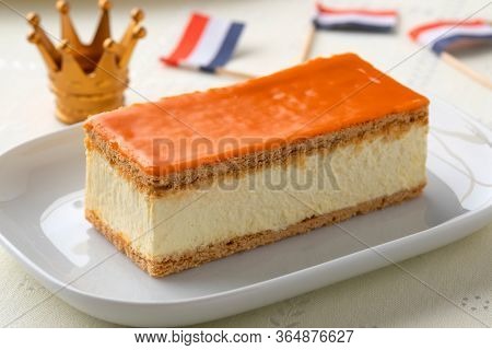 Traditional Dutch orange Tompouce pastry for kings day with crown and flag on the background