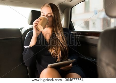 Young Attractive Businesswoman In Black Dress Sitting On Back Seat In Car With The Tablet In Hand Dr