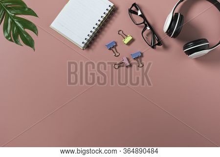 Top View With The Glasses, Note Book And Headphone On Pink Backgroup. Cluttered Office Desk Backgrou