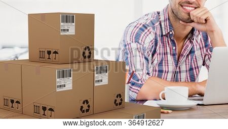 Mid section of a happy Caucasian man using laptop computer at home shopping on line with pile of cardboard parcel boxes next to him. Online shopping ecommerce social distancing and self isolation in