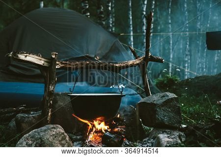 Kettle On Fire Near Tent In Forest At Night. Beautiful Campfire In Tourist Camp Into Wild. Survival 