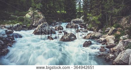 View Of Robust Water Flow In Small Stream With Boulders Trees And Forest Landscape.