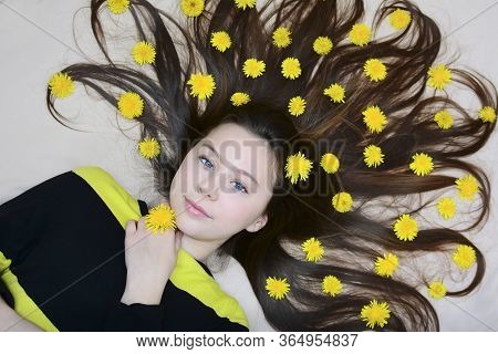 Portrait Of A Young Girl With Yellow Dandelion Flowers In Her Loose Hair. Top View