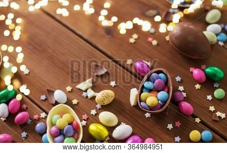 easter, sweets and confectionery concept - chocolate eggs and candy drops on wooden background