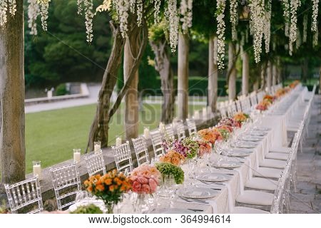 Wedding Dinner Table Reception. A Very Long Table For Guests With A White Tablecloth, Floral Arrange