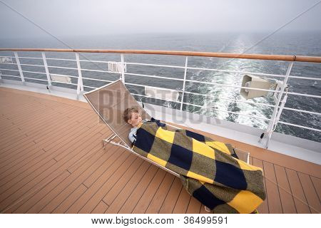 Little boy dormendo sul lettino coperto di coperta a bordo nave passeggeri grande, messa a fuoco sul ragazzo