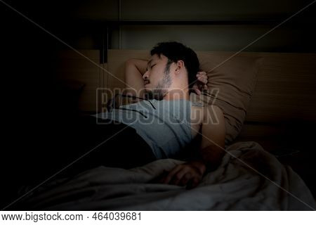 Handsome Asian Young Man Sleeping Cozily On A Bed In His Bedroom At Night.