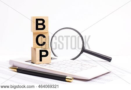 On A White Calculator, Next To A Magnifying Glass And A Black Pen, Wooden Cubes Marked Bcp Business 